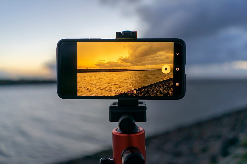 A smartphone mounted on a tripod filming a sunset, illustrating iPhone camera and video evolution
