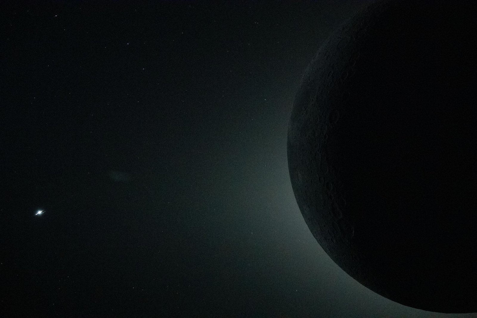 Crescent Moon photographed during NASA's Artemis II crewed lunar flyby in April 2026, with Earth visible as a distant point of light