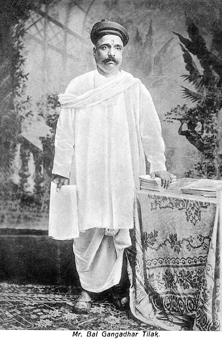 Bal Gangadhar Tilak standing beside a table with books, in a turban and white shawl, c. 1905