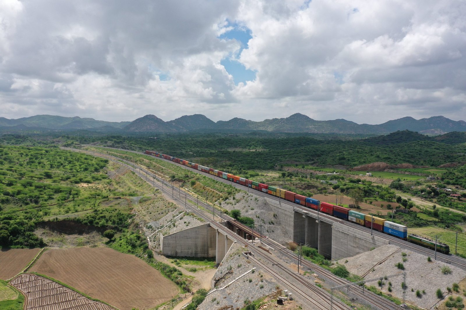 A double-stack container freight train running on an elevated section of India's Western Dedicated Freight Corridor