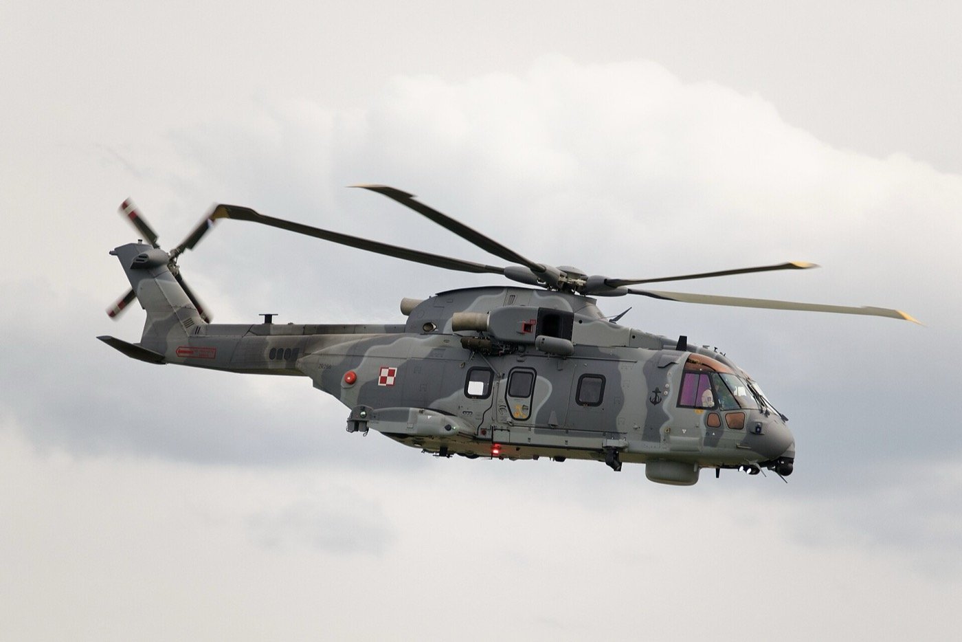 AgustaWestland AW101 three-engine helicopter in grey camouflage flying against a cloudy sky