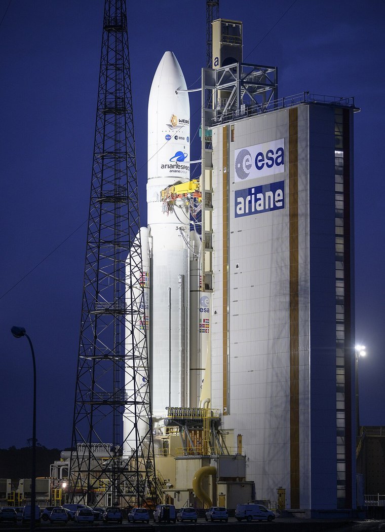 An Ariane 5 rocket carrying the James Webb Space Telescope on its launch pad at dusk with the ESA and Ariane logos visible on the launch tower