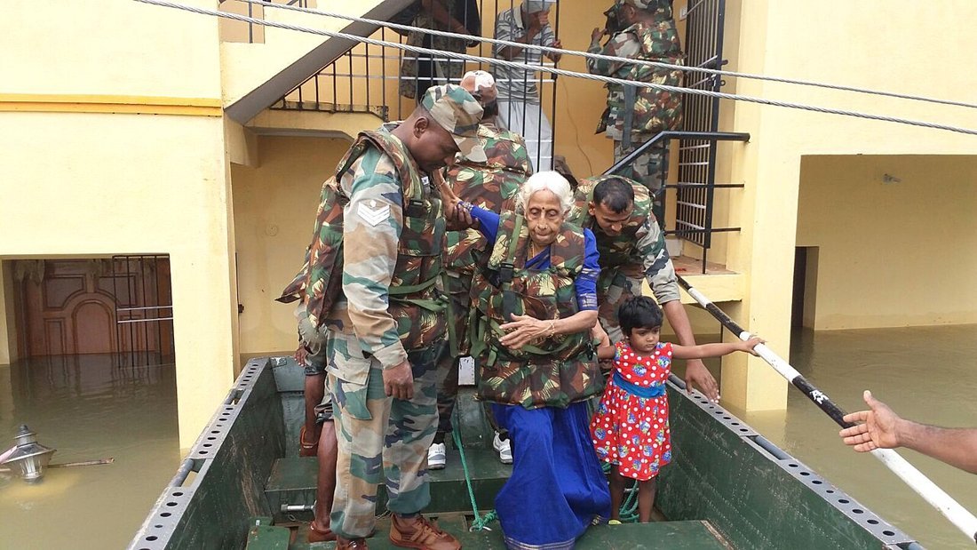 Soldiers in camouflage helping an elderly woman and a young girl onto a boat from a flooded building