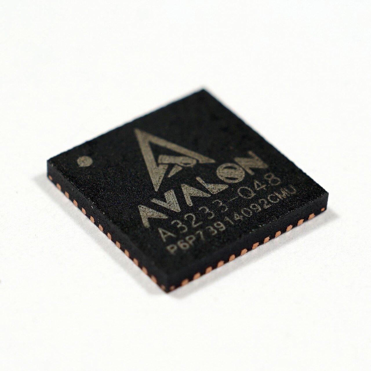 Close-up of a black Avalon A3233 mining chip with gold lettering on a white background