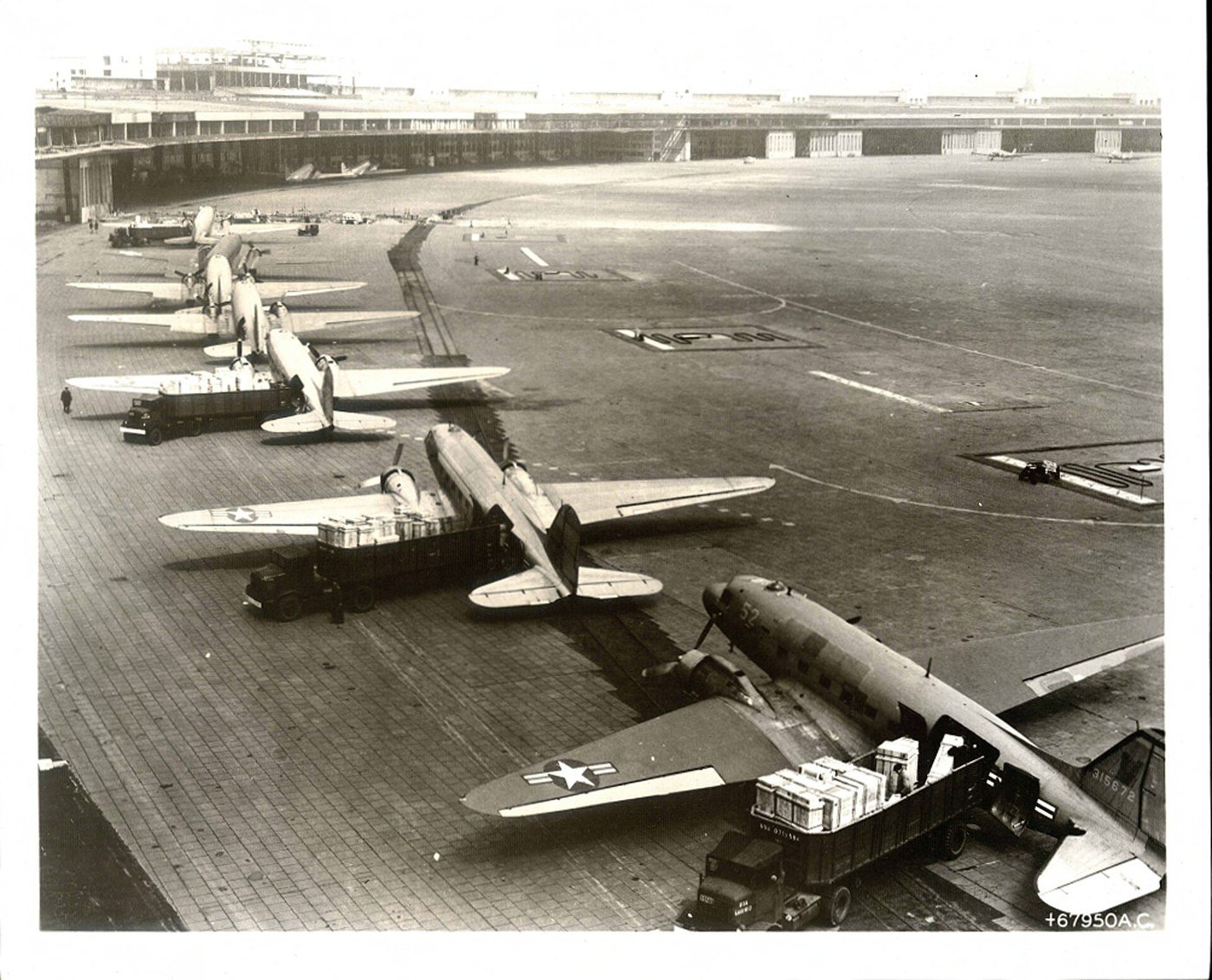 A line of C-47 transport aircraft being unloaded on the apron at Tempelhof with the terminal building behind