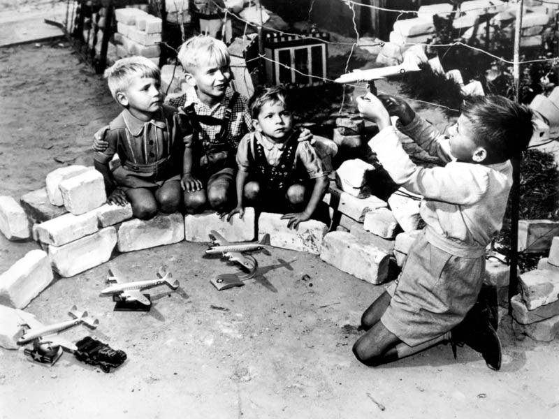 Berlin children kneeling in rubble holding toy aircraft in a game of airlift