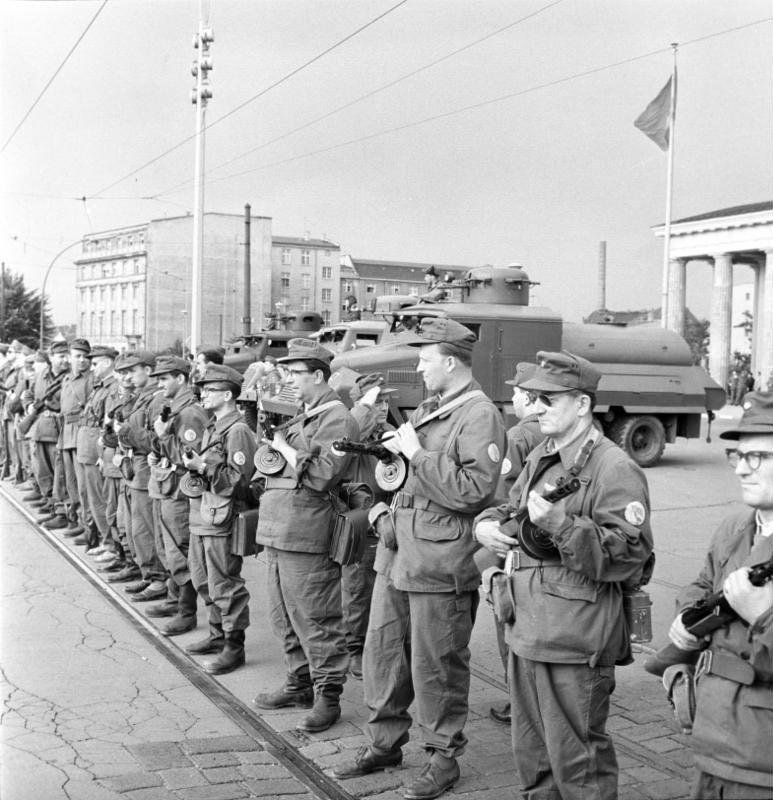 Armed East German militia men standing in a line beside a water cannon vehicle near the Brandenburg Gate on the day the border was sealed
