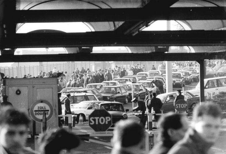 Black-and-white photograph of cars queuing and people waiting at the Bornholmer Straße border crossing with a STOP sign and customs booth