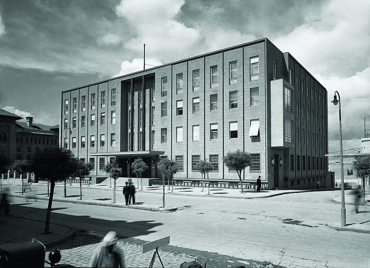 Black-and-white photograph of a four-storey stone central bank building with young trees in front