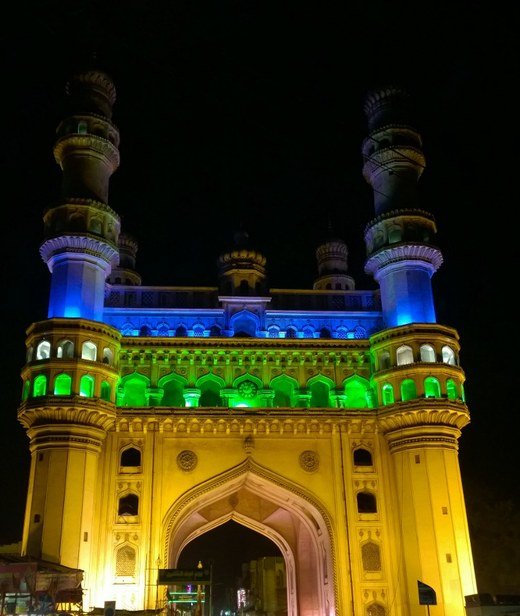 The Charminar monument in Hyderabad at night, its minarets and arches lit in saffron, white and green