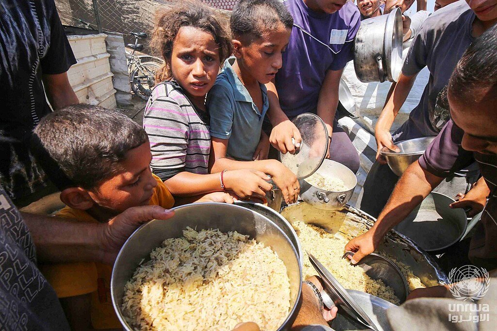 Children in Deir el-Balah hold out pots for cooked food from a charity kitchen in August 2024
