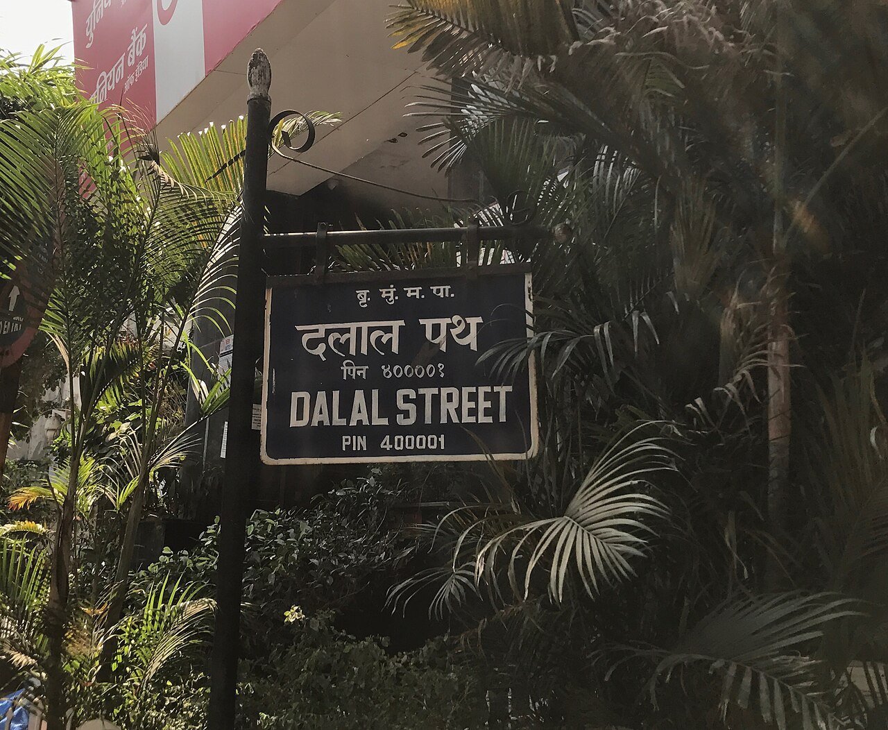 A black Dalal Street sign in Hindi and English with pin code 400001 among tropical foliage