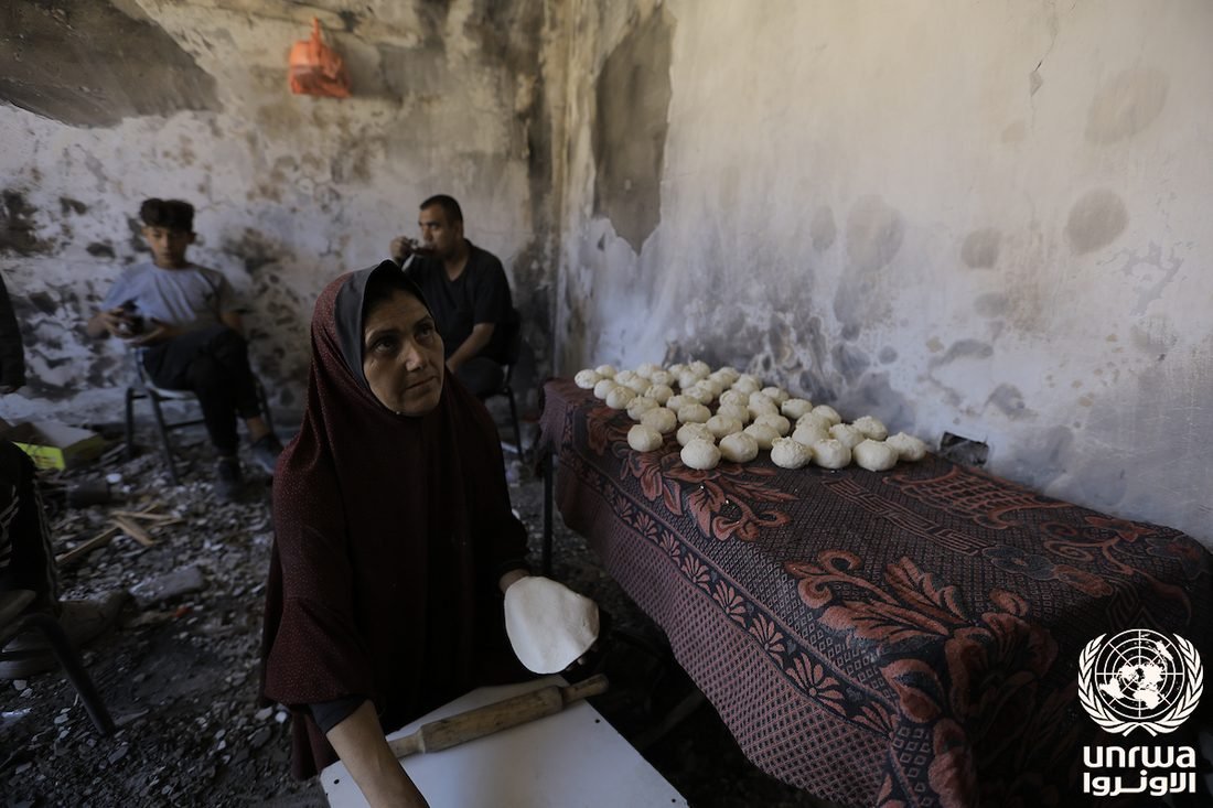 A displaced woman in Gaza prepares bread dough from flour gathered by hand