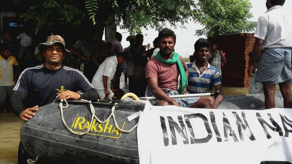 Indian Navy personnel on an inflatable boat marked Indian Navy among residents in floodwater