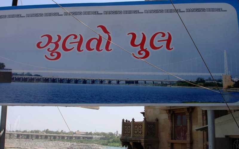 A signboard reading Jhulto Pul in Gujarati script with a picture of the bridge on the Machchhu River