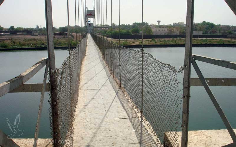 Looking along the narrow deck of the Morbi suspension bridge between mesh railings over the river