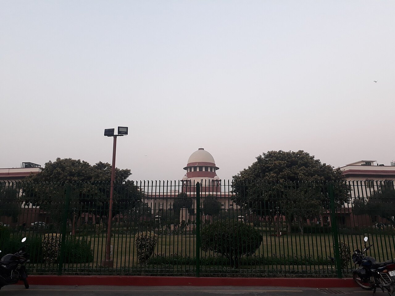 The dome of the Supreme Court of India seen behind a black iron fence and trees in New Delhi